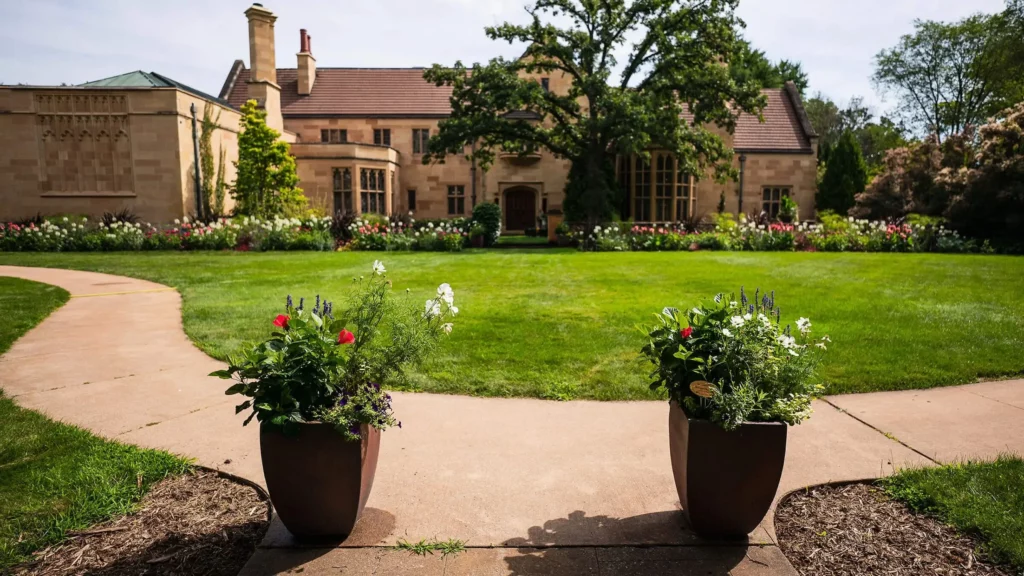 The façade of the Paine mansion in summertime, with two planters and blooming pink and white flowers.