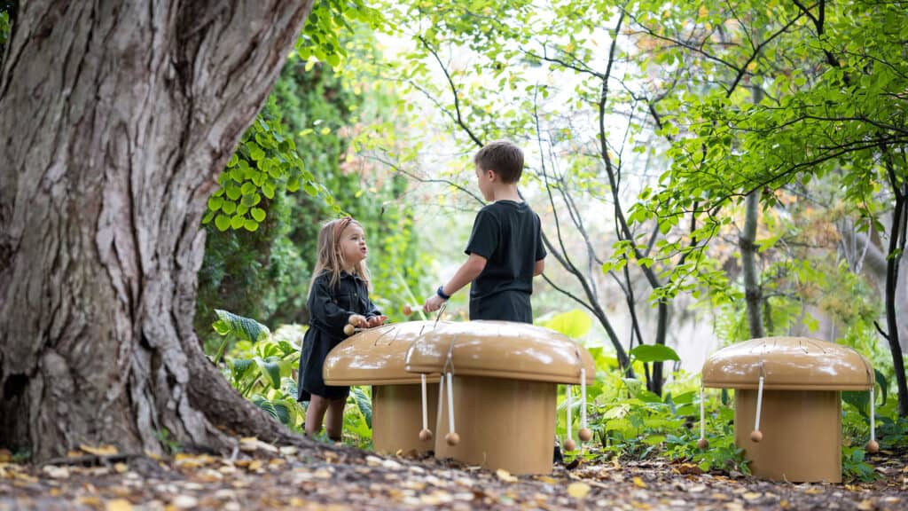 Children play with mushroom-shaped marimbas amid greenery and tress in the Children’s Garden.