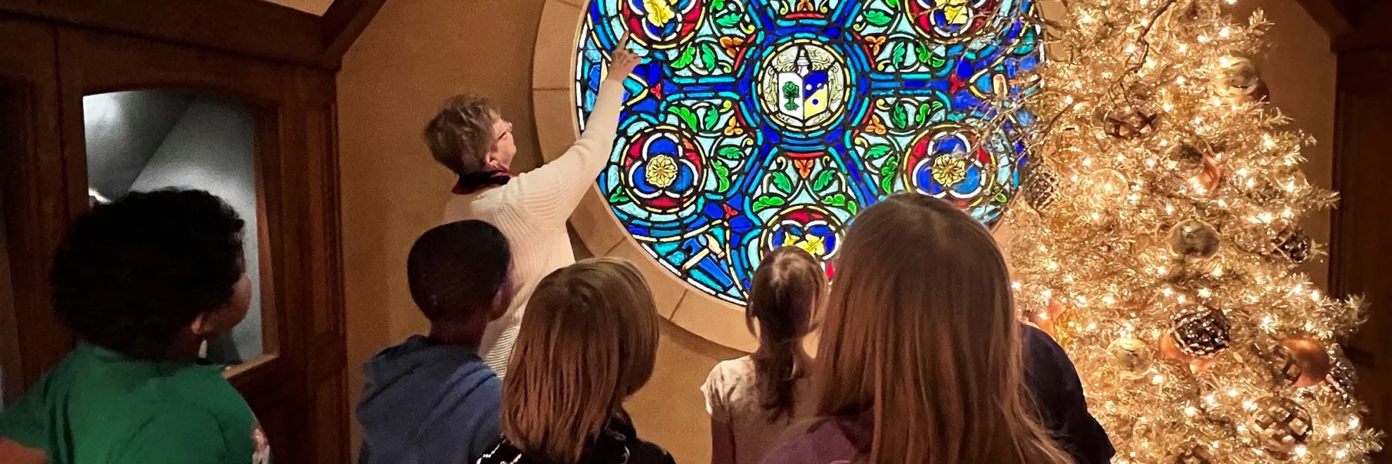 Children view a stained-glass window with a volunteer during the Christmas season.