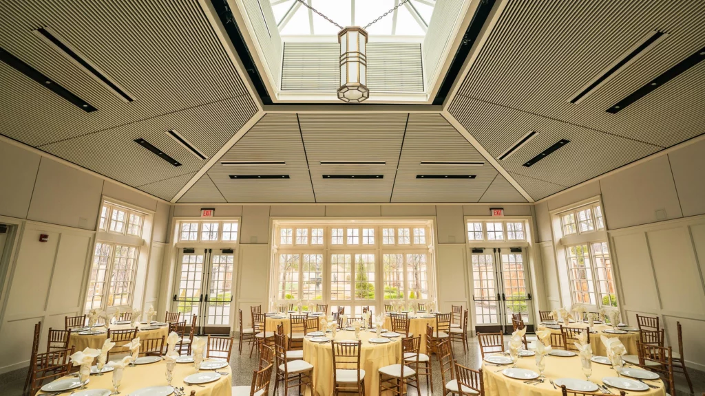 The Conservatory set up for an event with a yellow theme and round tables. 