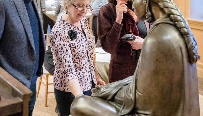 Three people view a sculpture up close.