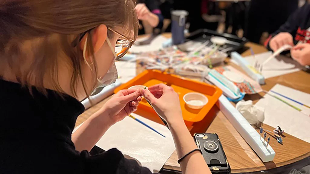 A girl creates a bead using magazine paper and toothpicks.