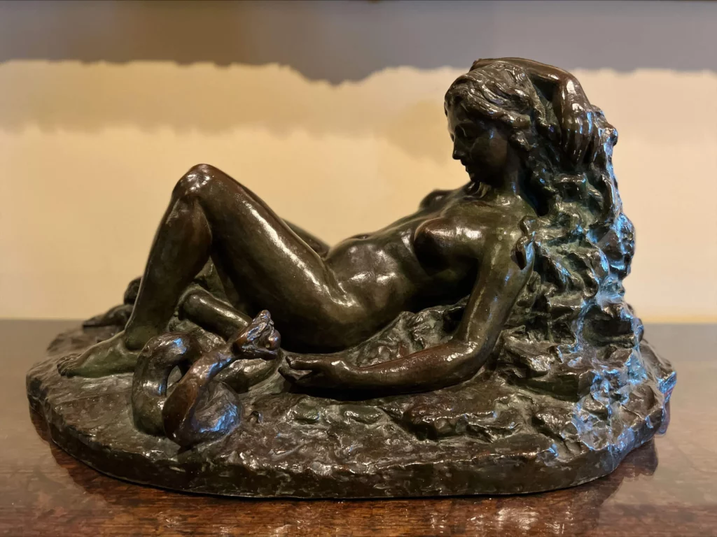 A sculpture of Eve in a reclining position, pondering to accept the forbidden fruit offered by the serpent.
