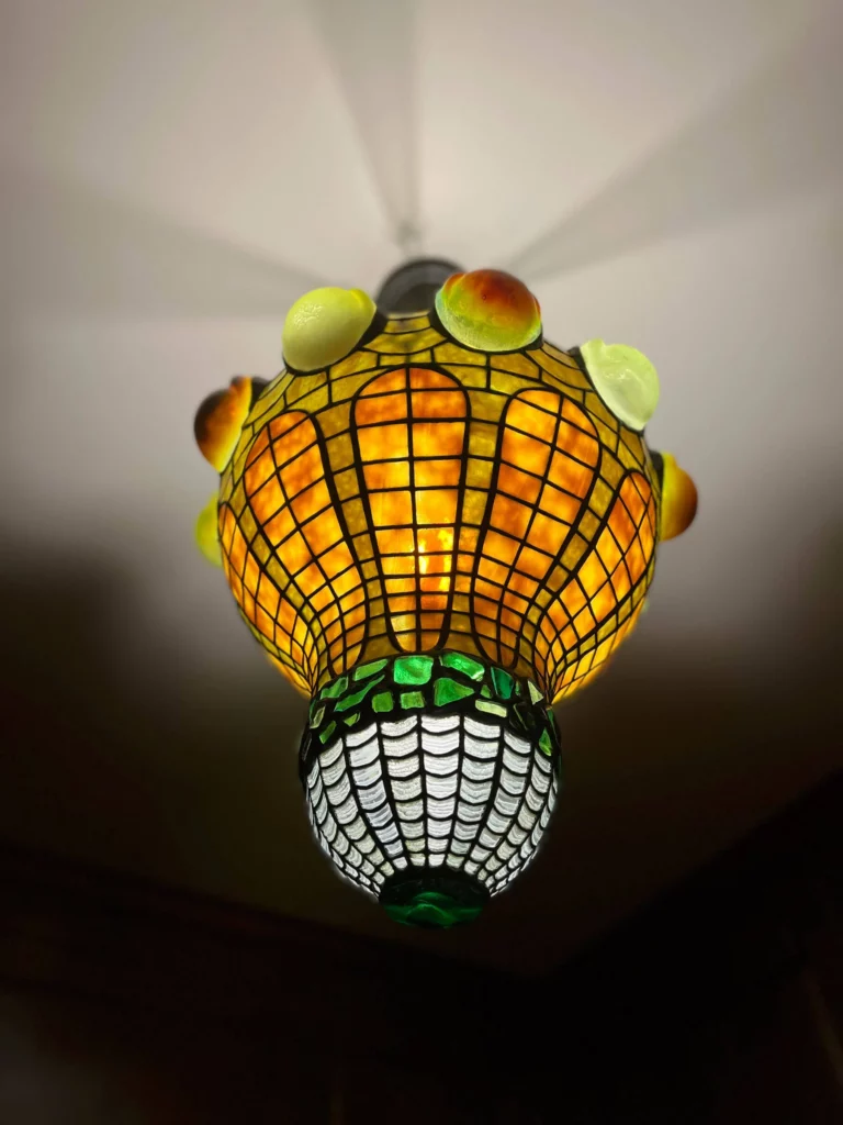 A yellow and green leaded glass chandelier with geometric patterns and opalescent, blown-glass teardrop jewels.