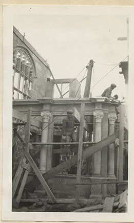 A construction worker poses while kneeling on scaffolding to construct a portion of the Breakfast Room.