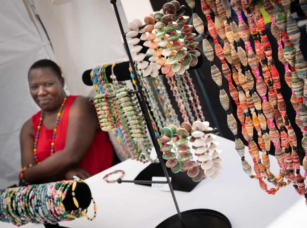 A woman selling beaded bracelets smiles to the camera while in her vendor booth.