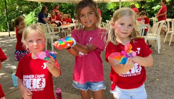 Three girls pose for a photo with craft butterflies they created.