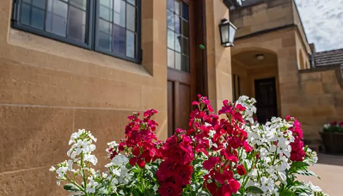 A planter with pink and white flowers stands next to the mansion in spring