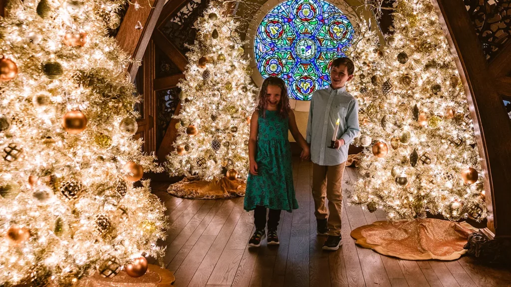 Two children walk among golden Christmas trees in the Gothic Gallery.