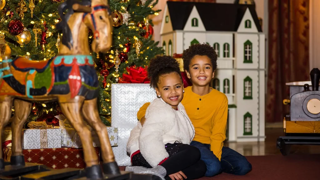 Two children pose for a photo in front of the giant Christmas tree in the Opening Party Scene.