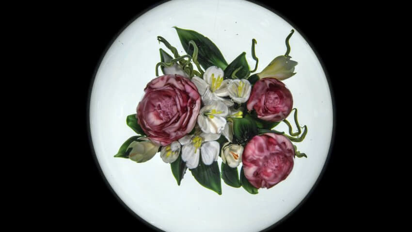 A paperweight with pink roses, white accent flowers, and greenery.