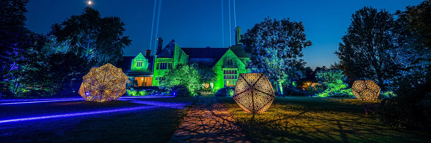 The Great Lawn of the Paine illuminated in green, blue, and yellow lighting, with three large geometric sculptures.