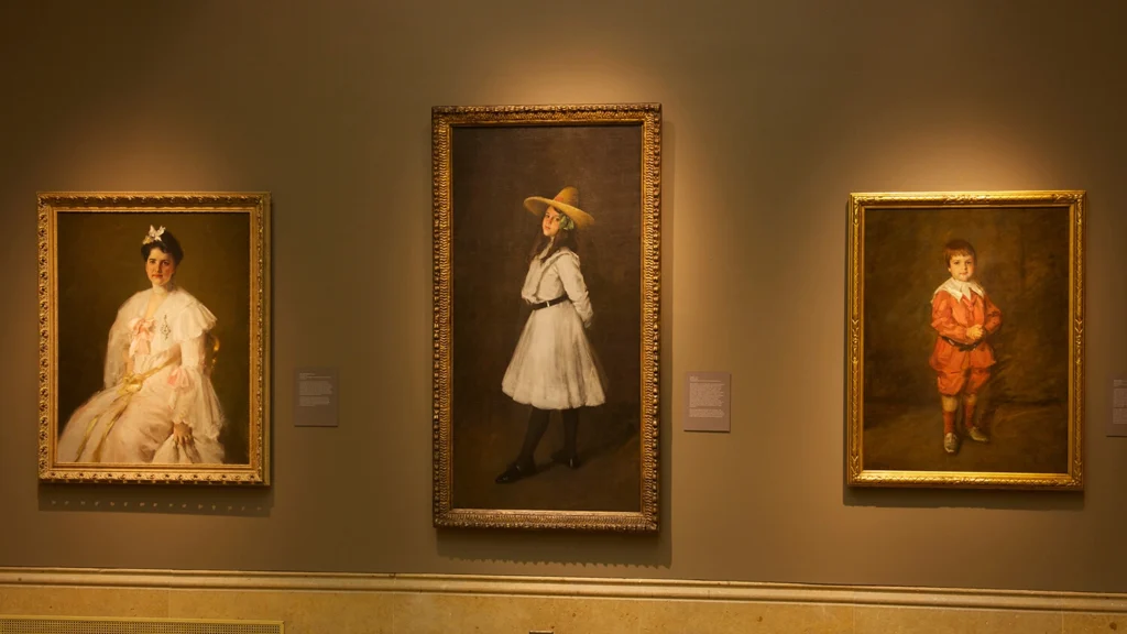 Artworks by William Merritt Chase hang on a wall.