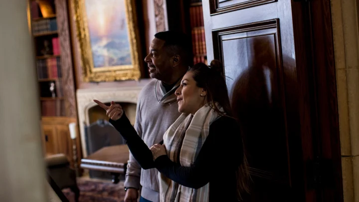 Two people point at artwork in the mansion.