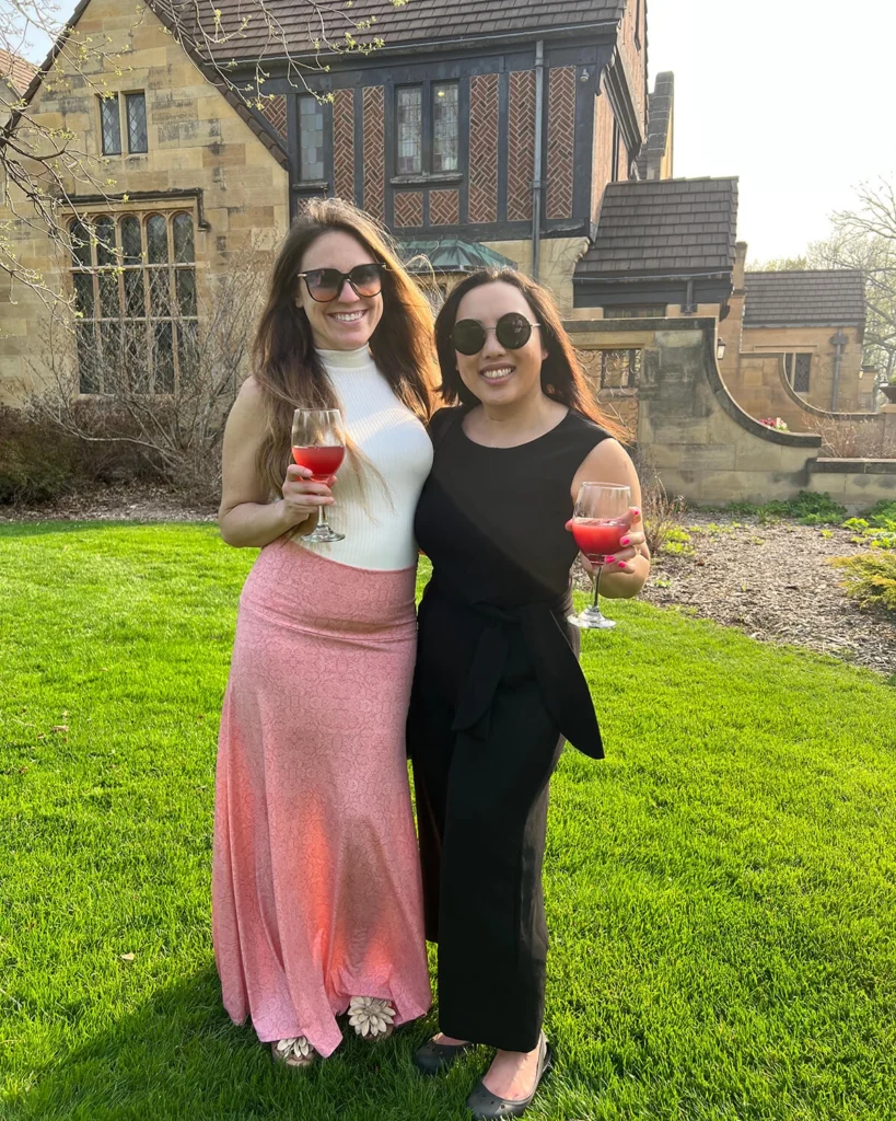 Two women with wine glasses pose for a photo in the gardens.