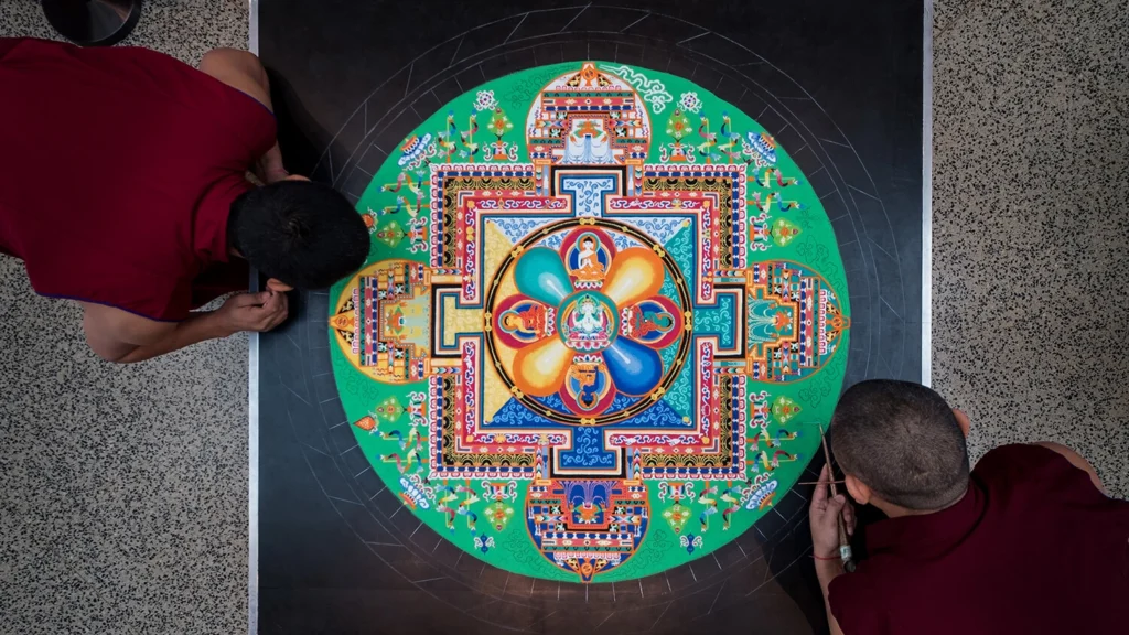 Two Tibetan monks work on a sand mandala.