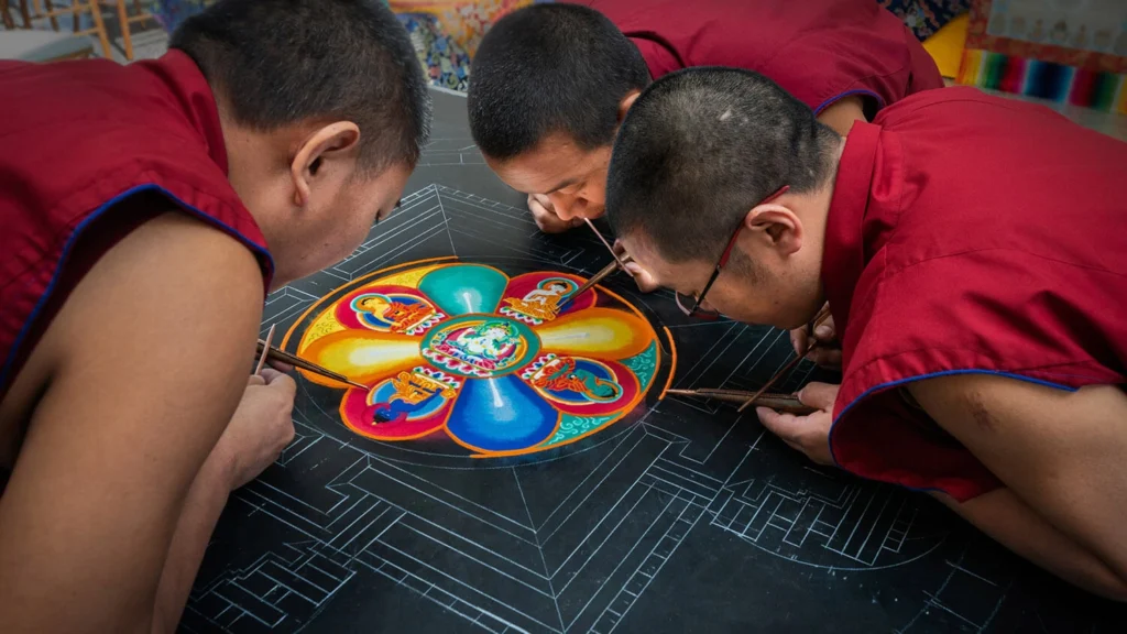 Three Tibetan monks work on a sand mandala.