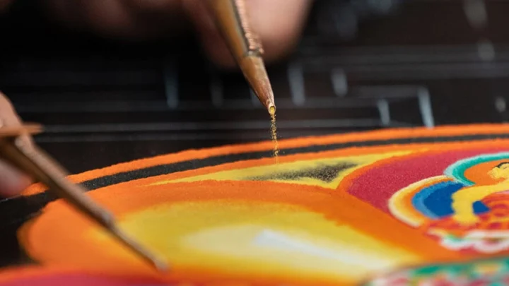 A funnel and striker disperse sand to create a mandala.