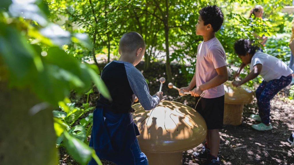Children play mushroom-shaped drums in the gardens at the Paine.