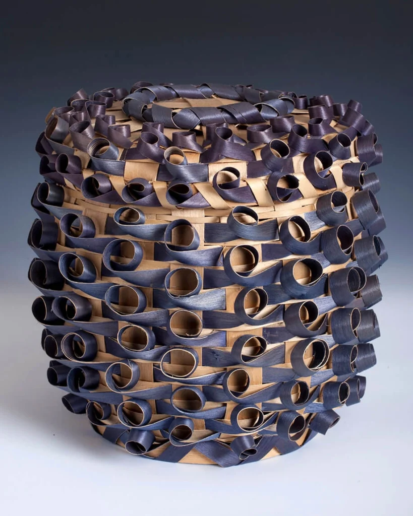 A black ash basket with curly Qs and a lid created by Helen Lonetree.