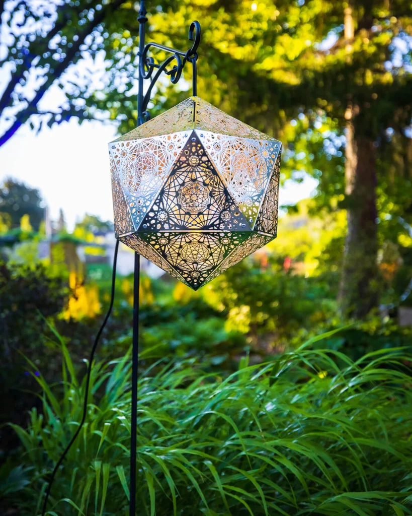 A metal geometric sculpture surrounded by blooming gardens.