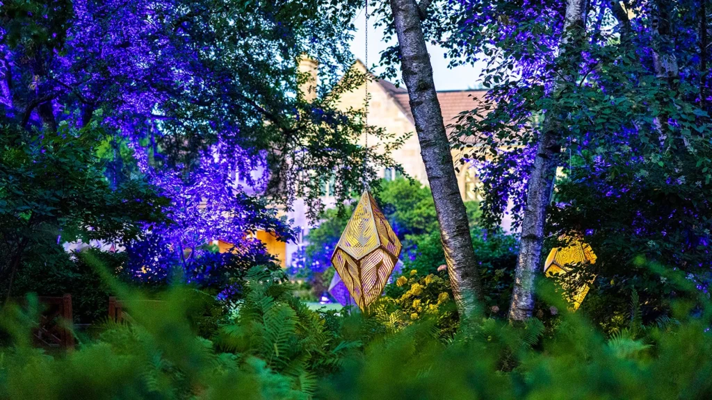 Metal geometric sculptures surrounded by blooming gardens.