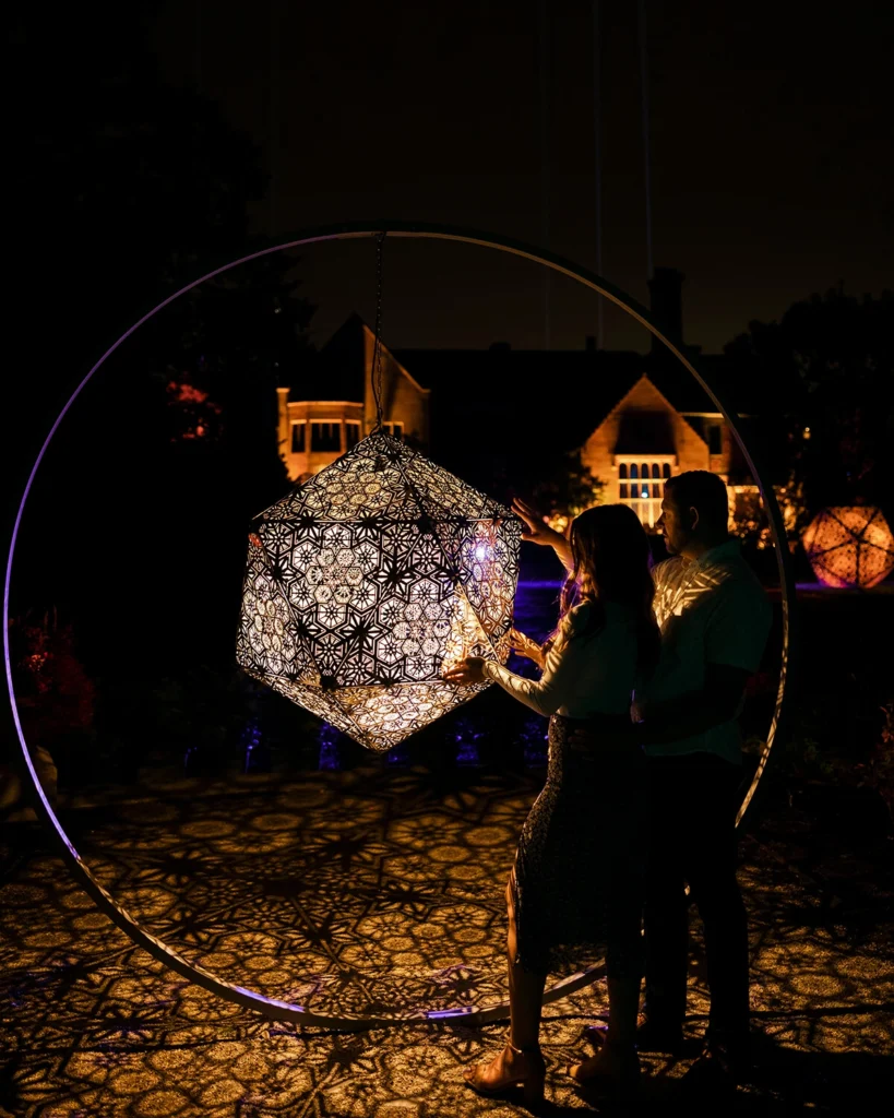 A couple plays with a lighted geometric sculpture at night.