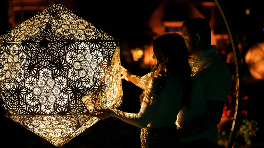 A couple plays with a lighted geometric sculpture at night.